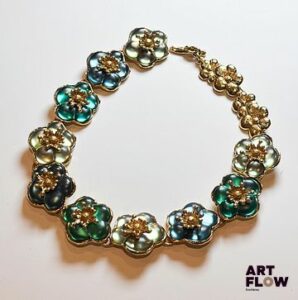KENZO Collier en métal doré à décor de fleurs stylisées, les pétales des fleurs centrales dans les tons verts Longueur 33 cm Partie manquante (chaine et fermoir)