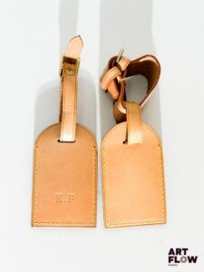 LOUIS VUITTON Deux étiquettes de bagage en cuir naturel marron clair dont l'une monogrammée des initiales "K.F." Très bon état général, quelques imperfections dont une tache masquée par la lanière.